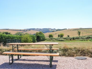 An outdoor picnic table with benches on a gravel area surrounded by grass and hills at Semira Tent Lodge in Blackawton