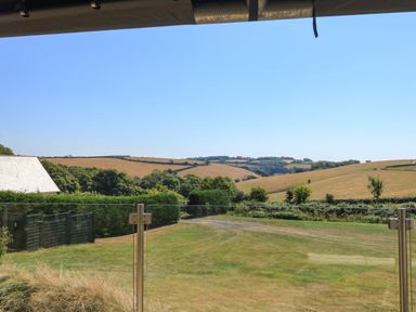 A view of rolling hills and fields with hedges and trees seen from a glass balcony at Semira Tent Lodge in Blackawton