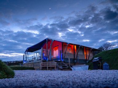 A lit tent lodge at dusk with outdoor seating and a barbecue grill at Semira Tent Lodge in Blackawton