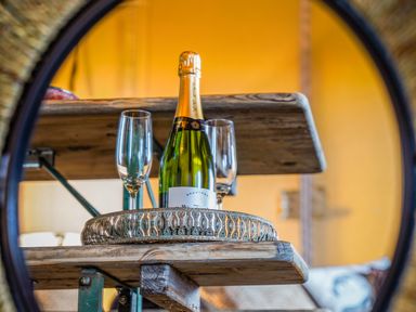 A bottle of champagne and two champagne glasses on a decorative tray on a wooden table at Semira Tent Lodge in Blackawton
