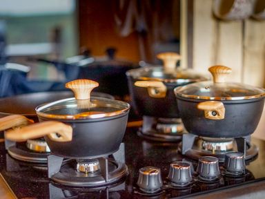 A kitchen stove with three black pots with wooden handles and lids at Semira Tent Lodge Blackawton