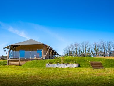 An outdoor tent structure with a deck and chairs on a grassy hill with stairs and a planter box at Semira Tent Lodge in Blackawton