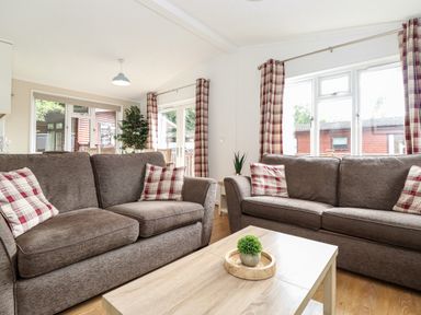A living room with two brown sofas with plaid cushions and a wooden coffee table at Honeysuckle Lodge in Thirlmere 14 White Cross Bay near Windermere