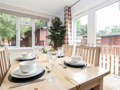 A dining table with place settings and glasses next to large windows and a potted plant at Honeysuckle Lodge Thirlmere 14 White Cross Bay near Windermere