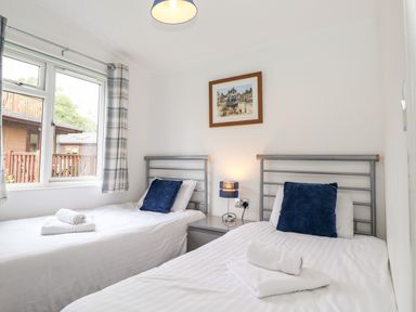 A bedroom with two single beds blue pillows and folded towels by a window at Honeysuckle Lodge in Thirlmere 14 White Cross Bay near Windermere
