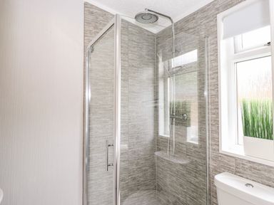 A bathroom with a glass shower enclosure a showerhead a window with a plant and a toilet at Honeysuckle Lodge in Thirlmere 14 White Cross Bay near Windermere