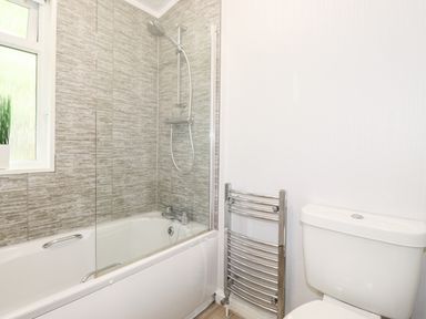 A bathroom with a bathtub and shower, a towel warmer, a toilet, and a window with a plant at Honeysuckle Lodge in Thirlmere 14 White Cross Bay near Windermere