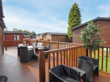 An outdoor wooden deck with black wicker chairs a dining table and a potted plant at Honeysuckle Lodge in Thirlmere 14 White Cross Bay near Windermere
