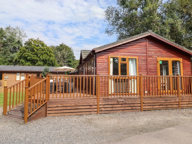 A wooden cabin with a deck and outdoor furniture at Honeysuckle Lodge in Thirlmere 14 White Cross Bay near Windermere