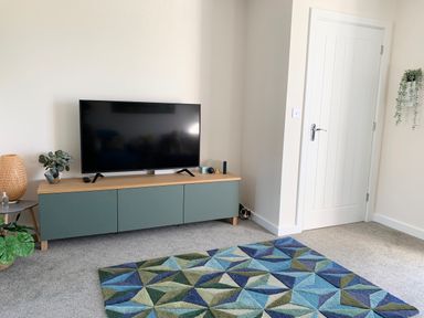A living room with a television on a cabinet and a geometric patterned rug on the floor at 2 Boathouse Terrace in Mawgan Porth