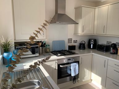 A kitchen with white cabinets stainless steel oven and stove a microwave kettle toaster and coffee machine at 2 Boathouse Terrace Mawgan Porth