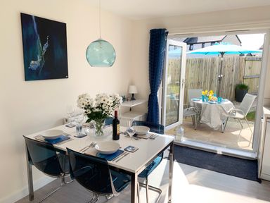A dining area with a table set for four and glass doors open to an outdoor patio with a table and chairs at 2 Boathouse Terrace in Mawgan Porth