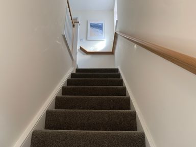 A carpeted staircase with wooden handrails and a framed picture on the wall at 2 Boathouse Terrace in Mawgan Porth