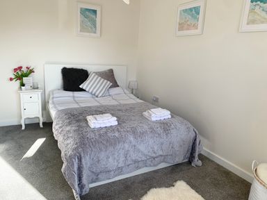 A bedroom with a bed with pillows and folded towels bedside tables with flowers and lamp framed pictures on the wall at 2 Boathouse Terrace in Mawgan Porth