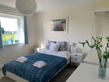 A bedroom with a bed covered by a blue blanket two bedside tables and a window with blue curtains at 2 Boathouse Terrace in Mawgan Porth
