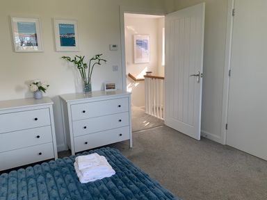 A bedroom with two white dressers plants on top and an open door leading to a hallway at 2 Boathouse Terrace in Mawgan Porth