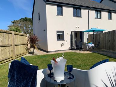 A backyard with a white two-story house patio table and umbrella and lawn chairs at 2 Boathouse Terrace in Mawgan Porth