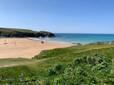 A sandy beach with red and yellow flags near the shoreline and grassy cliffs in the background at 2 Boathouse Terrace in Mawgan Porth