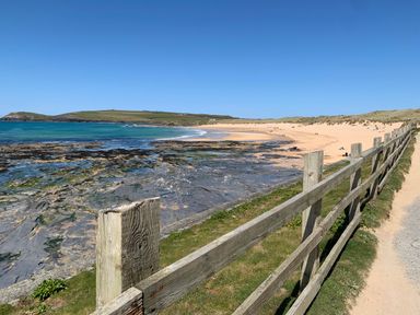 A sandy beach with rocks and a wooden fence along a pathway at 2 Boathouse Terrace in Mawgan Porth