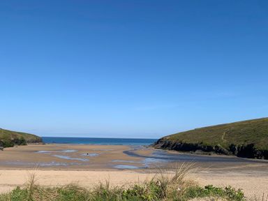 A beach with sand water hills and grass at 2 Boathouse Terrace in Mawgan Porth