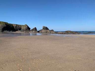 A sandy beach with rock formations and the ocean under a clear blue sky at 2 Boathouse Terrace in Mawgan Porth
