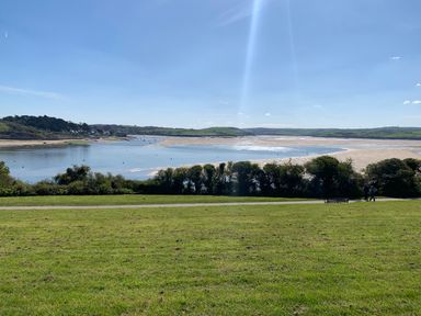 A river with sandbanks behind a grassy area and a pathway with two people walking at 2 Boathouse Terrace in Mawgan Porth