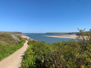 A coastal path with green bushes overlooking a river estuary and sandy beach at 2 Boathouse Terrace in Mawgan Porth