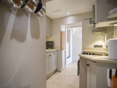 A narrow kitchen with beige cabinets a cooktop a cutting board and a dish rack at 1 Argyle House Lyme Regis