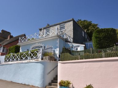 A two-story house with blue and pink painted walls and white fencing on a sunny day at 1 Argyle House in Lyme Regis