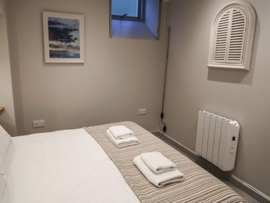 A bedroom with a bed with folded towels a radiator a small window and two wall decorations at 1 Argyle House in Lyme Regis