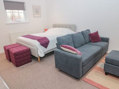 A bedroom with a bed gray sofa two purple ottomans and a window at Cherry Studio in Crookham near Cornhill-On-Tweed