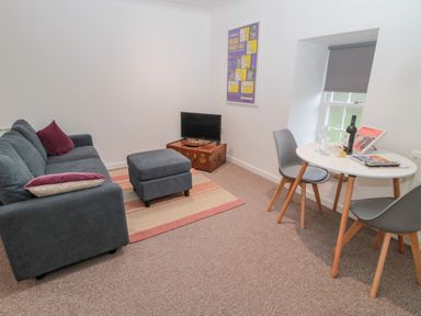 A living room with a sofa ottoman television on a vintage trunk dining table with chairs at Cherry Studio in Crookham near Cornhill-On-Tweed
