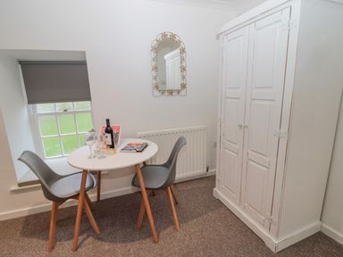 A small dining area with a round table and two chairs next to a window and a white wardrobe at Cherry Studio in Crookham near Cornhill-On-Tweed