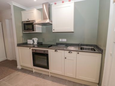 A kitchen with white cabinets a built in oven microwave electric stovetop kettle toaster and a sink at Cherry Studio in Crookham near Cornhill-On-Tweed