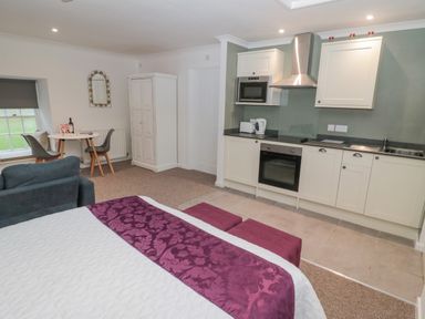 A studio room with a bed a kitchenette a small dining table with two chairs a wardrobe and a sofa at Cherry Studio in Crookham near Cornhill-On-Tweed