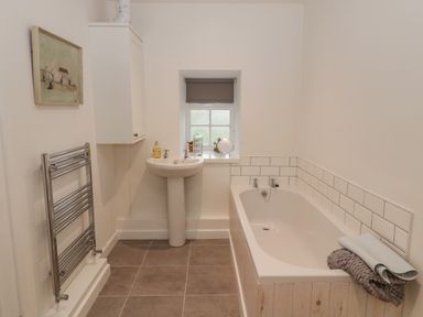 A bathroom with a bathtub a pedestal sink a towel radiator and a small window at Cherry Studio in Crookham near Cornhill-On-Tweed