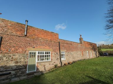 A brick and stone house with windows and a door on a grassy lawn at Cherry Studio in Crookham near Cornhill-On-Tweed