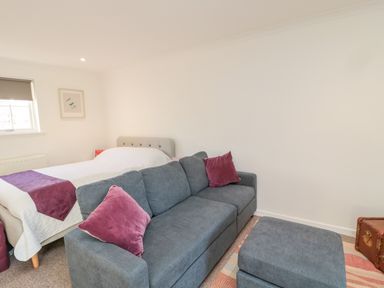 A bedroom with a bed and a grey sofa with purple cushions and an ottoman at Cherry Studio in Crookham near Cornhill-On-Tweed