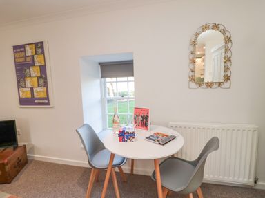 A small round table with two chairs near a window with a bottle, glasses, and books at Cherry Studio in Crookham near Cornhill-On-Tweed