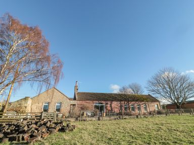 An exterior view of a single-story stone and brick building with windows and a patio area with chairs and tables at Cherry Studio in Crookham near Cornhill-On-Tweed