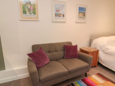 A brown sofa with two purple cushions beside a wooden bedside table and a bed with a white quilt at Silverbirch in Crookham near Cornhill-On-Tweed