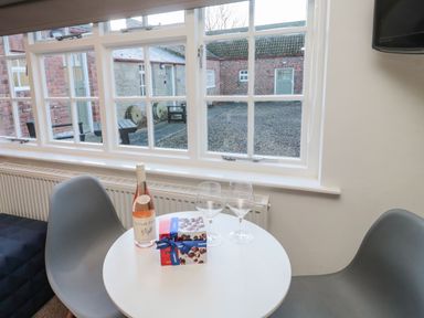 A small round table with a bottle of wine two wine glasses and a box of chocolates next to two chairs by a window at Silverbirch in Crookham near Cornhill-On-Tweed