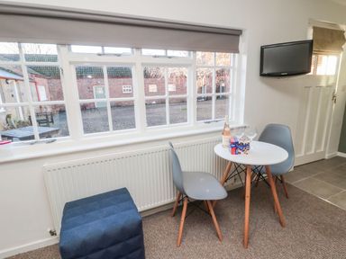 A small dining area with a round white table two gray chairs a blue stool a bottle of wine and two wine glasses by a window at Silverbirch in Crookham near Cornhill-On-Tweed