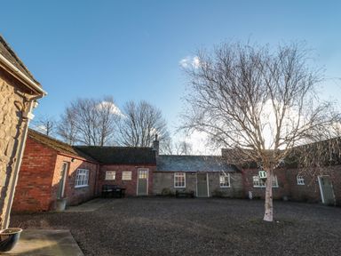 A courtyard with leafless trees surrounded by brick and stone buildings at Silverbirch in Crookham near Cornhill-On-Tweed