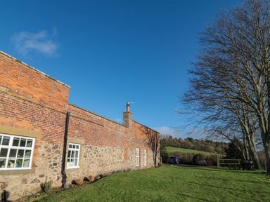 Exterior of a brick and stone building with windows a grassy lawn and trees at Silverbirch in Crookham near Cornhill-On-Tweed