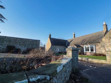 A stone house with chimneys and a low wall under a clear blue sky at Silverbirch in Crookham near Cornhill-On-Tweed