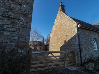 A wooden gate between stone buildings with a gravel path and leafless trees at Silverbirch in Crookham near Cornhill-On-Tweed