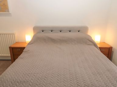 A bedroom with a bed covered with a quilt and two wooden bedside tables with lamps at Cheviot View in Crookham near Cornhill-On-Tweed