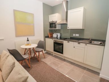 A kitchen with white cabinets, a stove, a sink, a small round dining table with two gray chairs and a sofa at Cheviot View in Crookham near Cornhill-On-Tweed