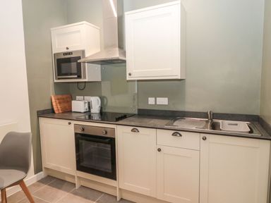 A kitchen with white cabinets a built in oven microwave a kettle toaster and a sink at Cheviot View in Crookham near Cornhill-On-Tweed